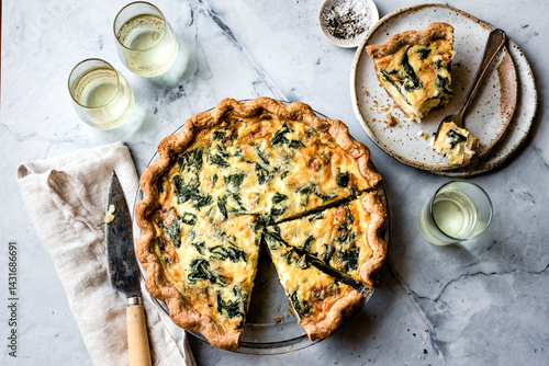 A delicious spinach quiche with a golden crust, served with a glass of white wine and a slice on a plate.