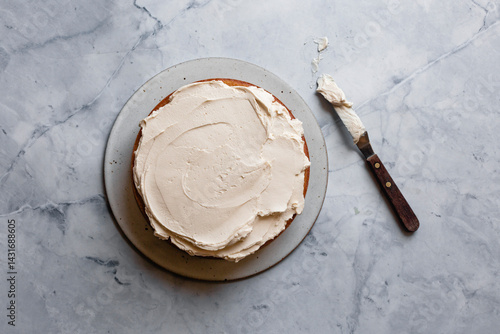 A cake with creamy frosting on a marble surface, accompanied by a butter knife.
