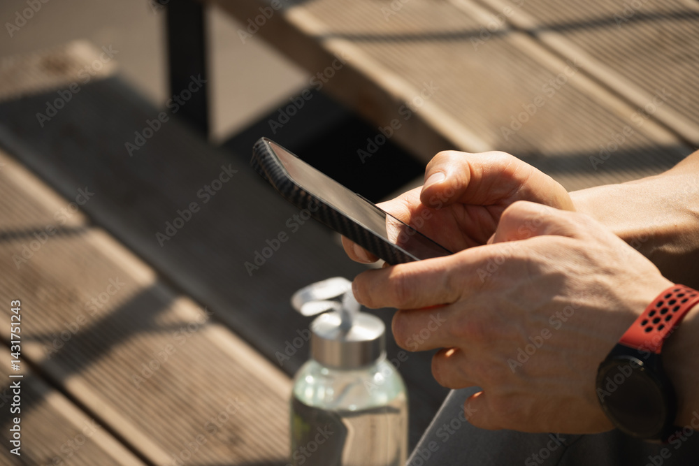 Smartphone in hands sporty man. Man sitting on stairs and check apps with water balance after training in heat weather. Summer season. Close up.