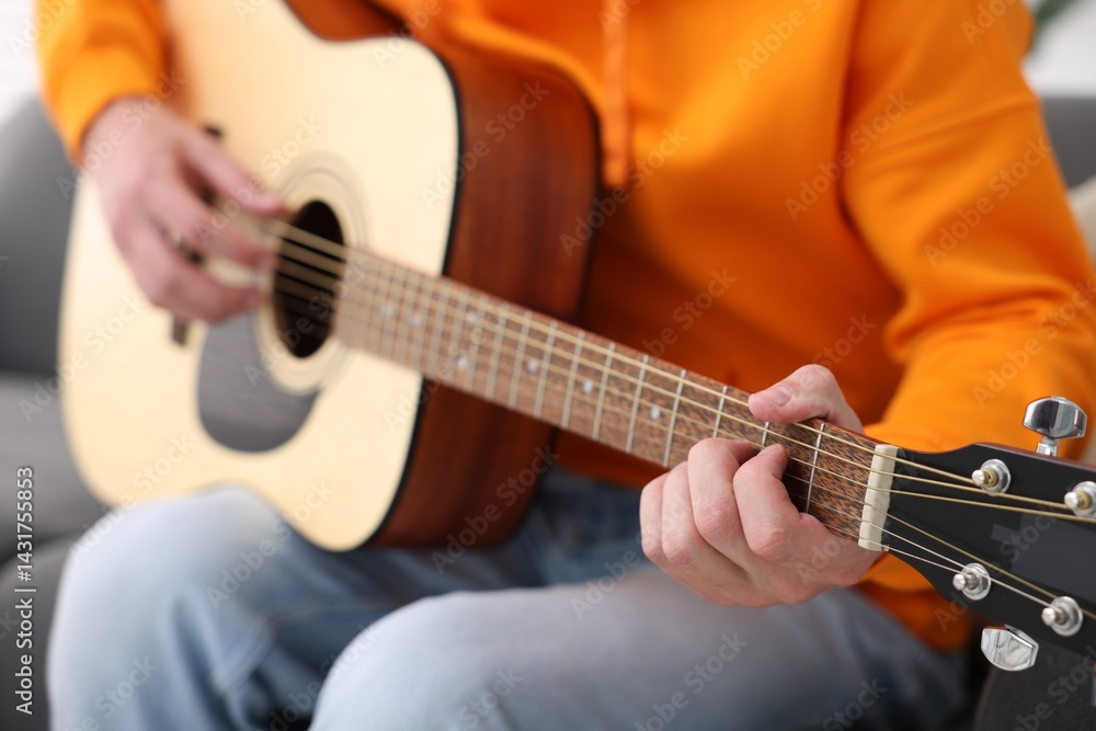 Fototapeta premium Young man playing guitar on sofa indoors, closeup