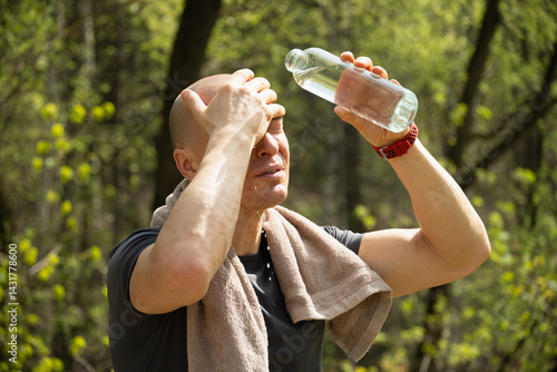 Obraz na płótnie Sporty adult caucasian man refreshing himself water from bottle against forest at summer heat after training outdoors. Water balance. Heat Danger. Overheating w salonie