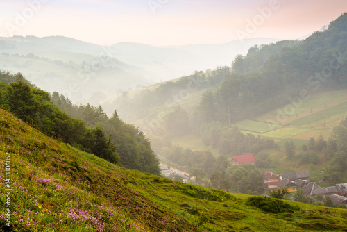 Obraz na płótnie abranka village in the valley at foggy sunrise. countryside landscape with red clouds above forested hills and rural fields. beautiful scenery of transcarpathia, ukraine in summer. open view w salonie