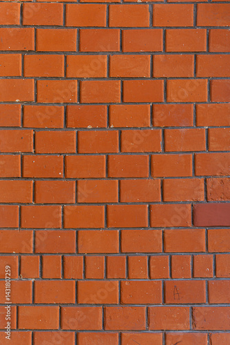 A brick wall with a red color. The wall is made of bricks. The bricks are arranged in a pattern