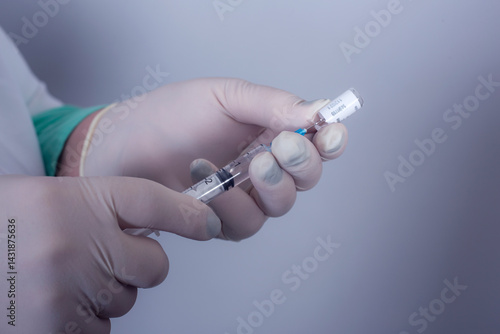 Doctor drawing up solution from vaccine bottle and filling syringe injection