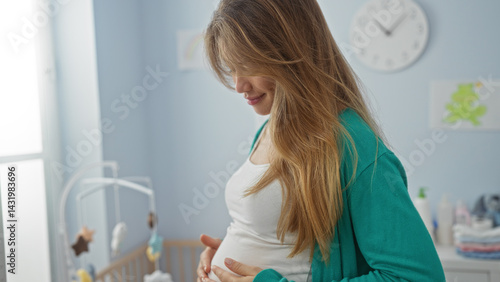 Obraz na płótnie Pregnant woman standing in bright bedroom affectionately holding her belly near a baby cradle with soft lighting and cozy atmosphere w salonie