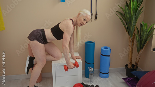Obraz na płótnie Woman exercising indoors with dumbbells in a gym setting featuring fitness equipment and plants, demonstrating strength and active lifestyle in a focused workout environment w salonie