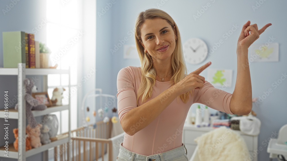 Woman smiling in bedroom pointing indoors, blonde female wearing casual clothes in cozy home environment with baby toys and nursery decor in bright daytime setting.