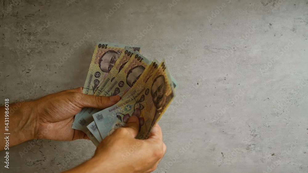 Man holding romanian lei bills against a concrete background, focusing on the colorful currency notes and their intricate details.