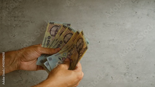 Obraz na płótnie Man holding romanian lei bills against a concrete background, focusing on the colorful currency notes and their intricate details. w salonie