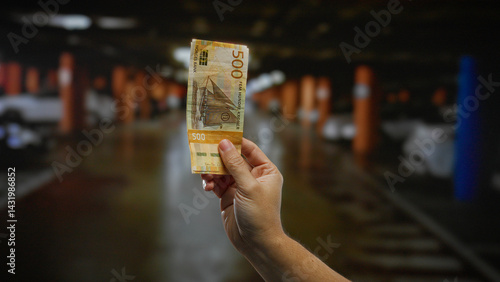 Obraz na płótnie Hand holding norwegian krone indoors with a blurred parking garage in the background, suggesting urban investment opportunities. w salonie