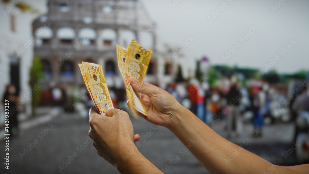 Hands holding philippine pesos in front of the roman coliseum, illustrating investment and travel themes in an urban outdoor setting.