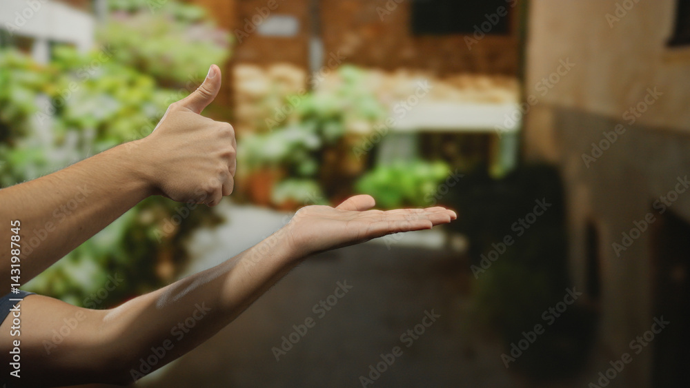 Man showing hands in a thumbs-up gesture on a city street, set against an urban outdoor backdrop with blurred greenery and buildings in a sunny setting.