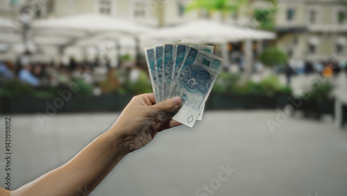 Obraz na płótnie Man holding polish zloty banknotes outdoors at a restaurant terrace, with city street and coffee patrons seen in the background, showcasing commerce in poland. w salonie