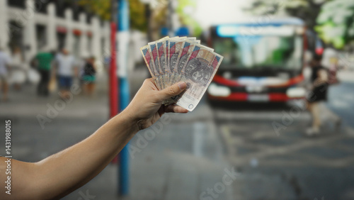 Obraz na płótnie Man holding polish zloty banknotes in hand at a bus stop, capturing the essence of urban polish life with people and public transport in the background. w salonie