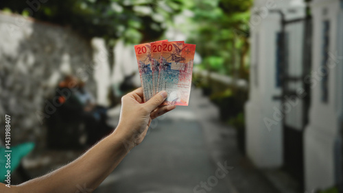 Obraz na płótnie Hand holding swiss francs on a city street, with a man visible in the blurred background, depicting an outdoor transaction or financial concept. w salonie