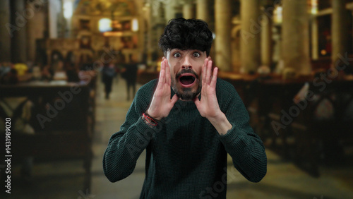 Obraz na płótnie Young man with surprised expressions in a historical church setting, wearing a sweater, showcasing emotions amid a blurred indoor backdrop. w salonie