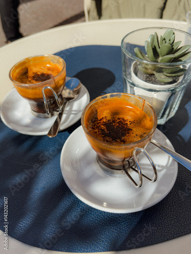 The small glass cup with Italian espresso (coffee) on a table with a saucer and a metal spoon 