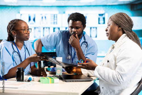 Black expert discussing with junior nurses to find the best treatment options, showcasing teamwork and professionalism in the healthcare industry. Improving the services at clinic.