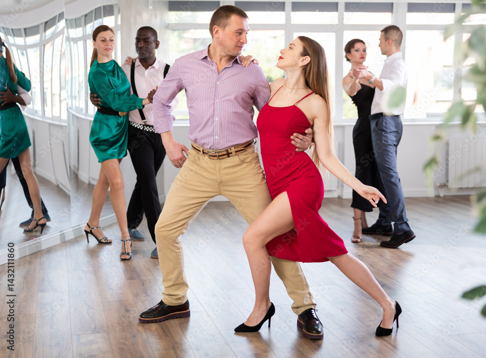 Fototapeta premium Dance training in group - men and women of different nationalities and different ages dance tango or bachata in a dance studio