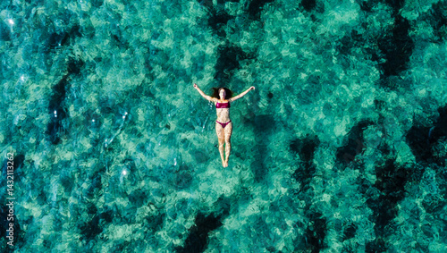 Minimalist aerial photograph taken by drone, showing a young woman in swimwear floating calmly in the bright blue Mediterranean waters