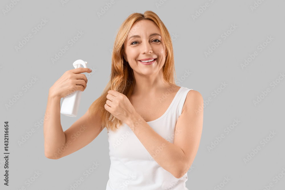 Mature woman applying hair care product on grey background Mature woman applying hair care product on grey background