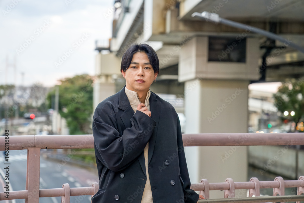 A Japanese man in his twenties wearing a black jacket is in Minato Mirai, Yokohama, Kanagawa Prefecture. He sits on a bench, gazing into the distance, surrounded by the calm mood of the modern city.