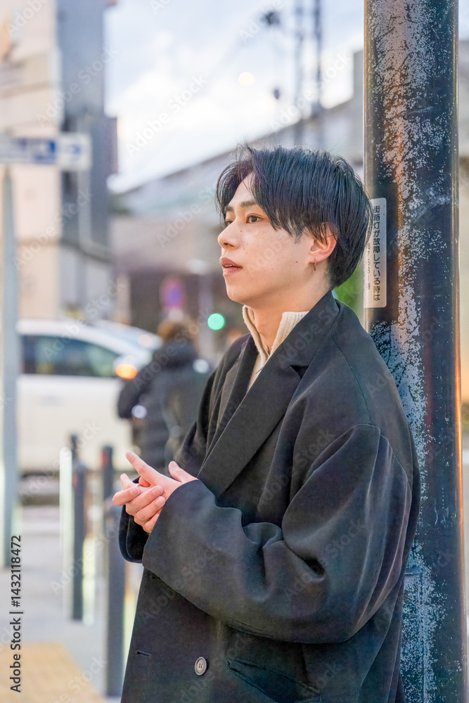 A Japanese man in his twenties wearing a black jacket is in Minato Mirai, Yokohama, Kanagawa Prefecture. He stands at a city intersection in the evening, surrounded by sunset light and urban scenery.