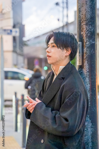 Obraz na płótnie A Japanese man in his twenties wearing a black jacket is in Minato Mirai, Yokohama, Kanagawa Prefecture. He stands at a city intersection in the evening, surrounded by sunset light and urban scenery. w salonie