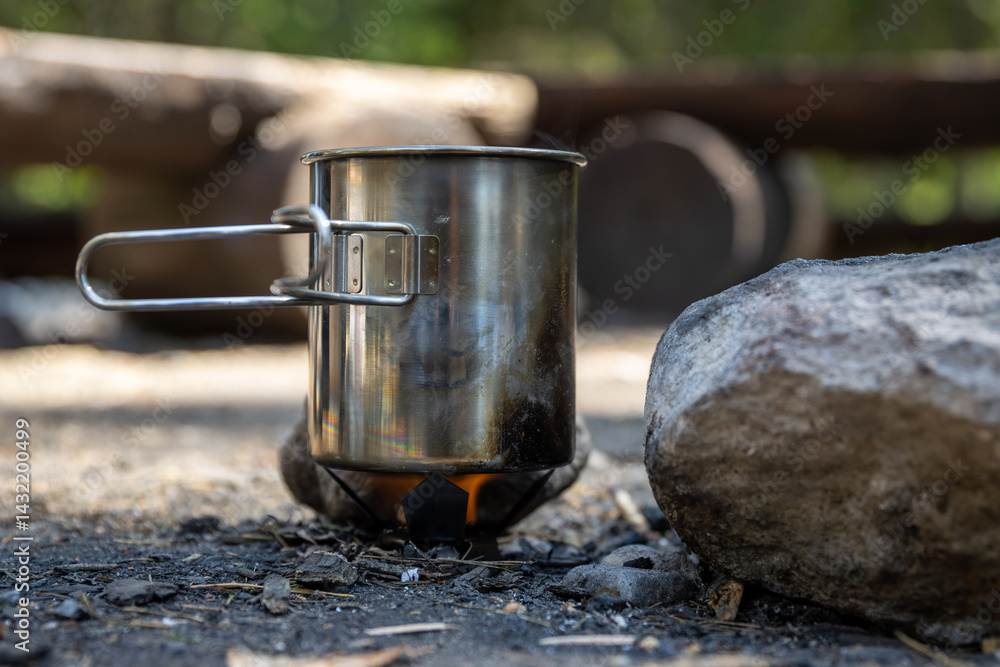 Heating water in a metal mug on a small burner. Making tea while hiking. Flame from a tablet with hexamine fuel tablet. Traveling and hiking in nature. Travel equipment for cooking.