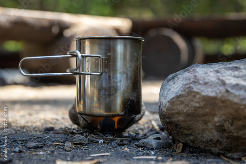Obraz na płótnie Heating water in a metal mug on a small burner. Making tea while hiking. Flame from a tablet with hexamine fuel tablet. Traveling and hiking in nature. Travel equipment for cooking. w salonie