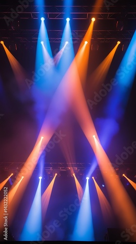 Vibrant stage lights in blue and orange beams shining through fog on dark concert stage, creating a dramatic atmosphere for entertainment, events, or performances

