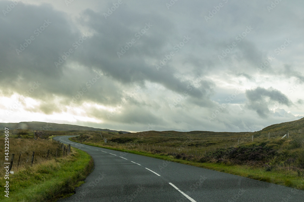 Fototapeta premium Winding roads cut through the natural wonders of the Isle of Skye: cliffs, rugged coastlines, and green hills shape a unique journey through wild beauty and unforgettable views