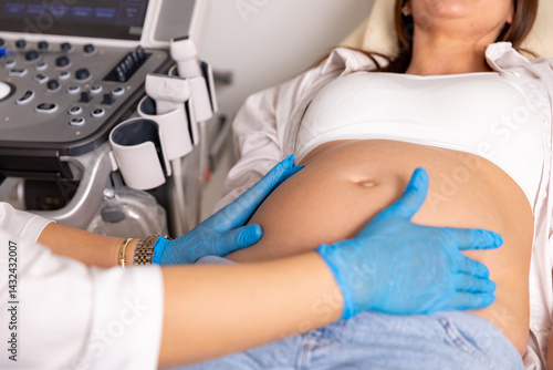 Obraz na płótnie Close up shot of female doctor examining pregnant woman lying on bed in clinic. Palpation of womb belly, feeling baby fetus embryo bumps. Gynecologist checkup w salonie