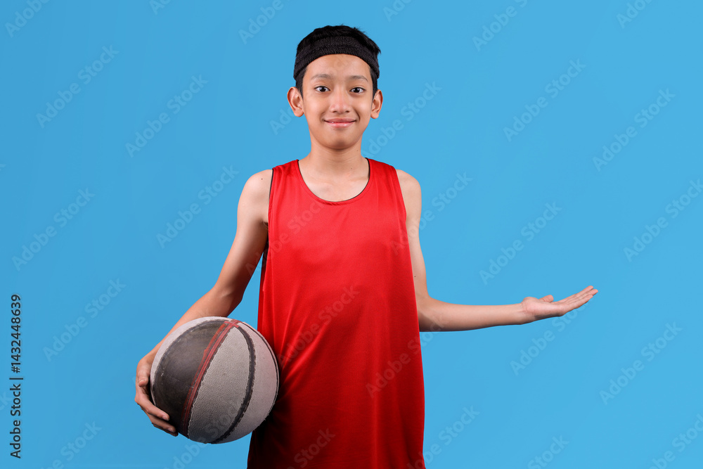Fototapeta premium Teenager boy holding basket ball and pointing with hand to the side isolated in blue background