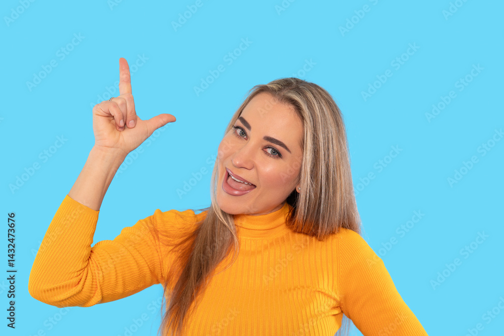 Fototapeta premium Smiling woman in a bright yellow sweater gestures playfully against a vivid blue background, expressing joy and energy during a casual moment
