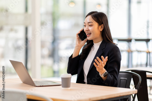 Happy young business woman manager talking consulting client on cell phone working on laptop in office. Busy woman professional business making call on cell using computer sitting at desk
