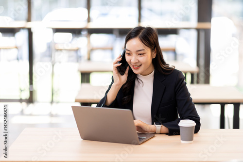 Happy young business woman manager talking consulting client on cell phone working on laptop in office. Busy woman professional business making call on cell using computer sitting at desk
