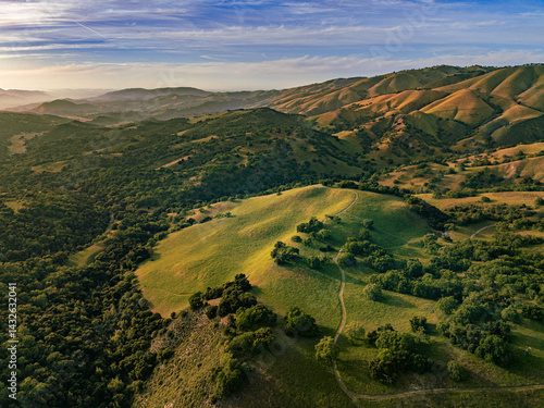 From above, a scenic view of deep Carmel Valley landscape of with green and golden rolling mountains under a cloudy sunset sky