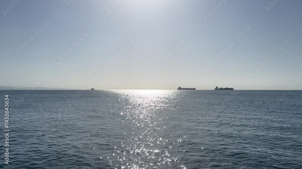 A Calm Serene View of the Ocean with Ships on the Horizon Under Bright Sunshine and Clear Blue Sky A Calm Serene View of the Ocean with Ships on the Horizon Under Bright Sunshine and Clear Blue Sky