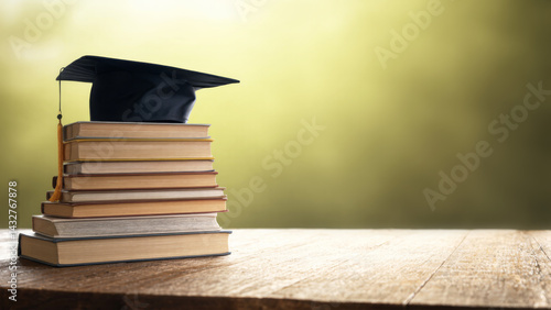 Obraz na płótnie Graduation cap on stack of books over blurred nature background. w salonie