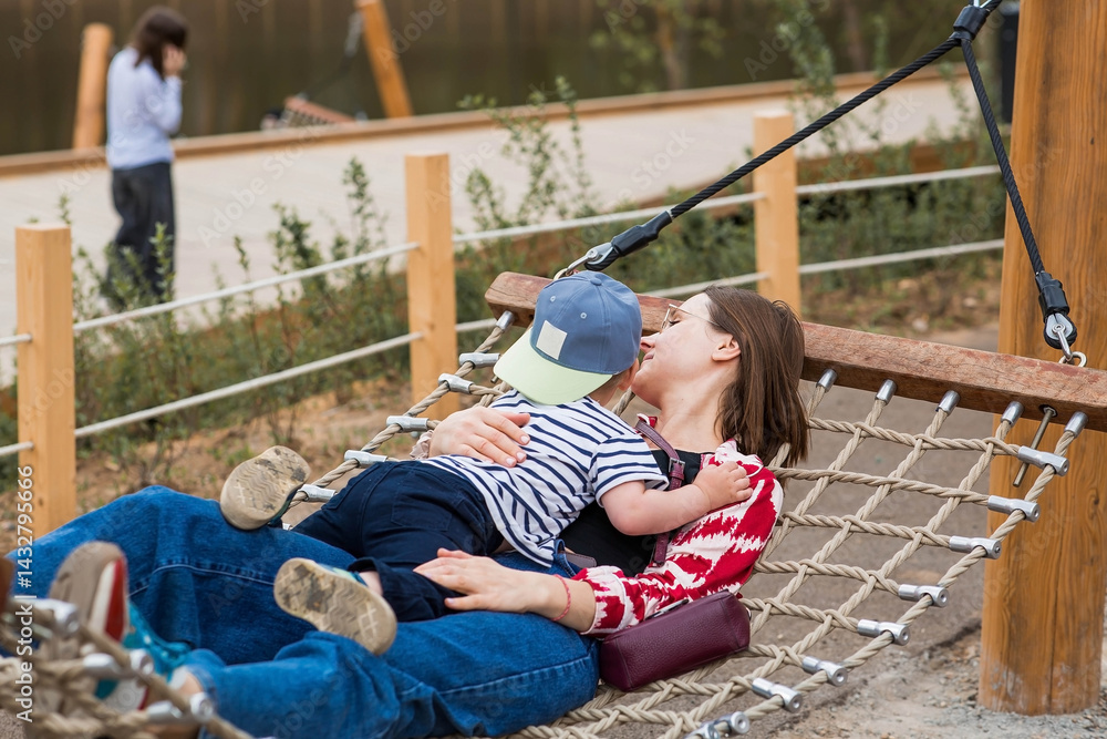 Lifestyle. A cute little boy and his mom are lying in a hammock on a modern outdoor playground. The concept of family privacy and entertainment.