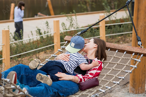 Obraz na płótnie Lifestyle. A cute little boy and his mom are lying in a hammock on a modern outdoor playground. The concept of family privacy and entertainment. w salonie