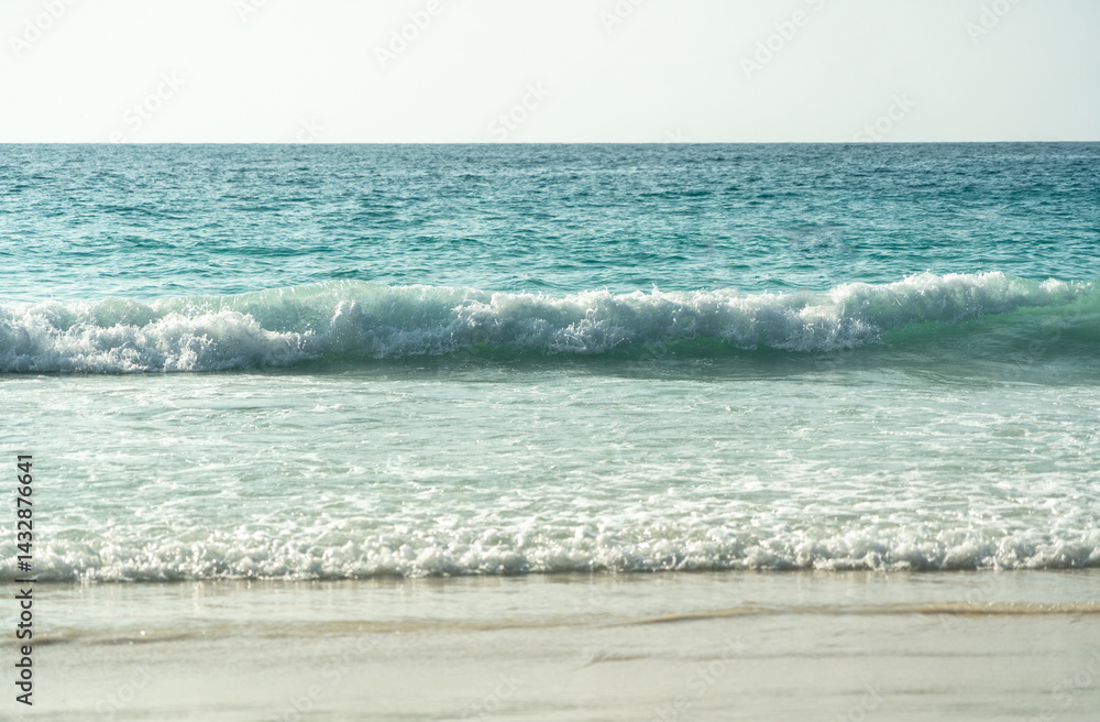 Clear turquoise waves gently crashing on a peaceful sandy beach at a tropical island coastline
