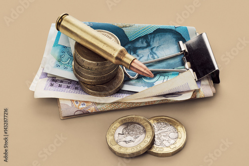 UK Defense Spending - still life of bullet cartridge and coins on stack of British money pounds
