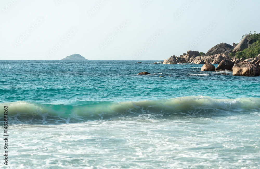Close-up texture of ocean waves and sandy beach under sunlight with turquoise tones and soft foam