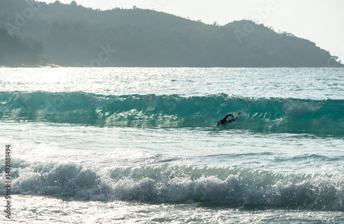 Obraz na płótnie A swimmer dives into a rolling turquoise wave in the Indian Ocean off a tropical Seychelles island w salonie
