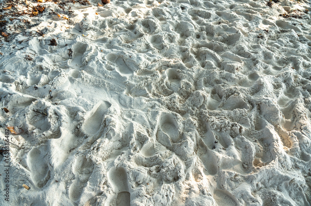 Close-up of white coral beach sand with footprints and soft shadows under tropical sunlight