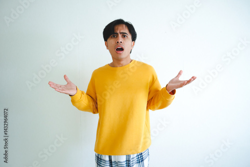 Foto Surprised Asian man raising both hands while looking at the camera with a confus