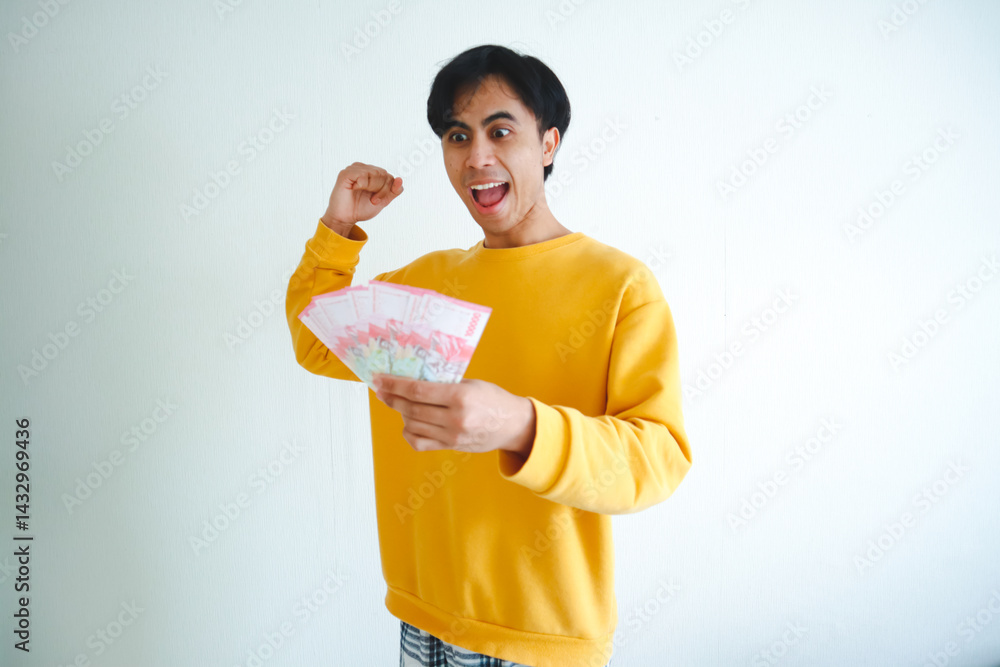 Excited Asian man holding lots of money celebrating success with joyful expression, isolated on white background Excited Asian man holding lots of money celebrating success with joyful expression, isolated on white background