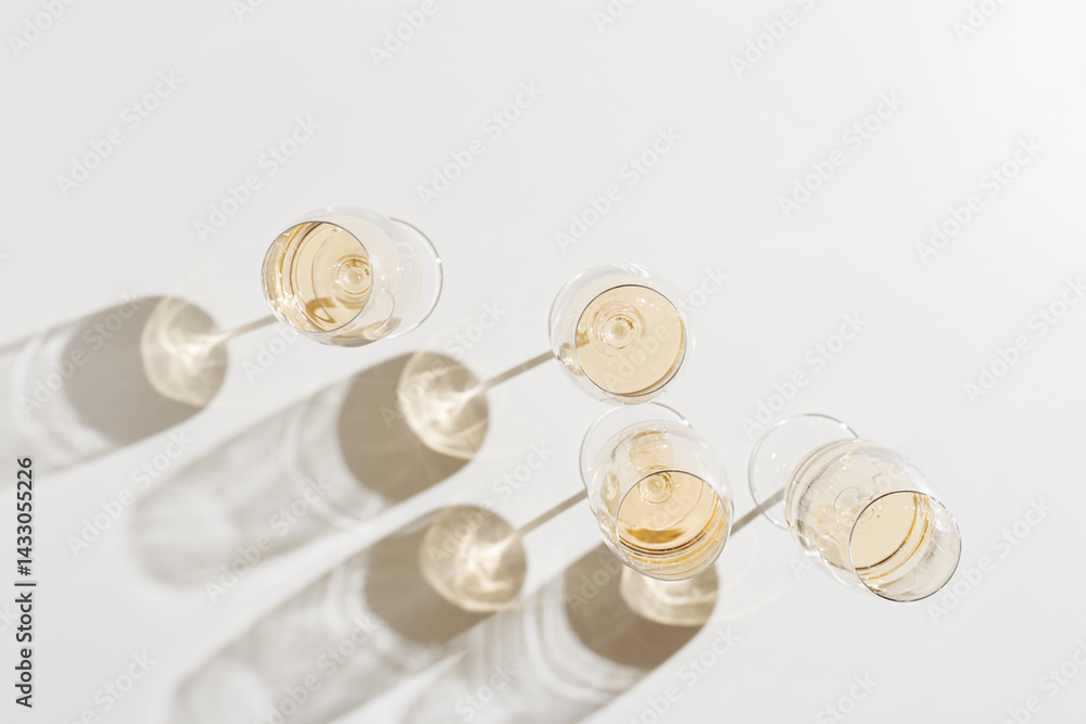 Many glasses of white wine, Aesthetic top view on white light background, minimal style flat lay. Wine glass at sunlight, sun shadows and shiny glare glass. Light alcohol drinks for party, events